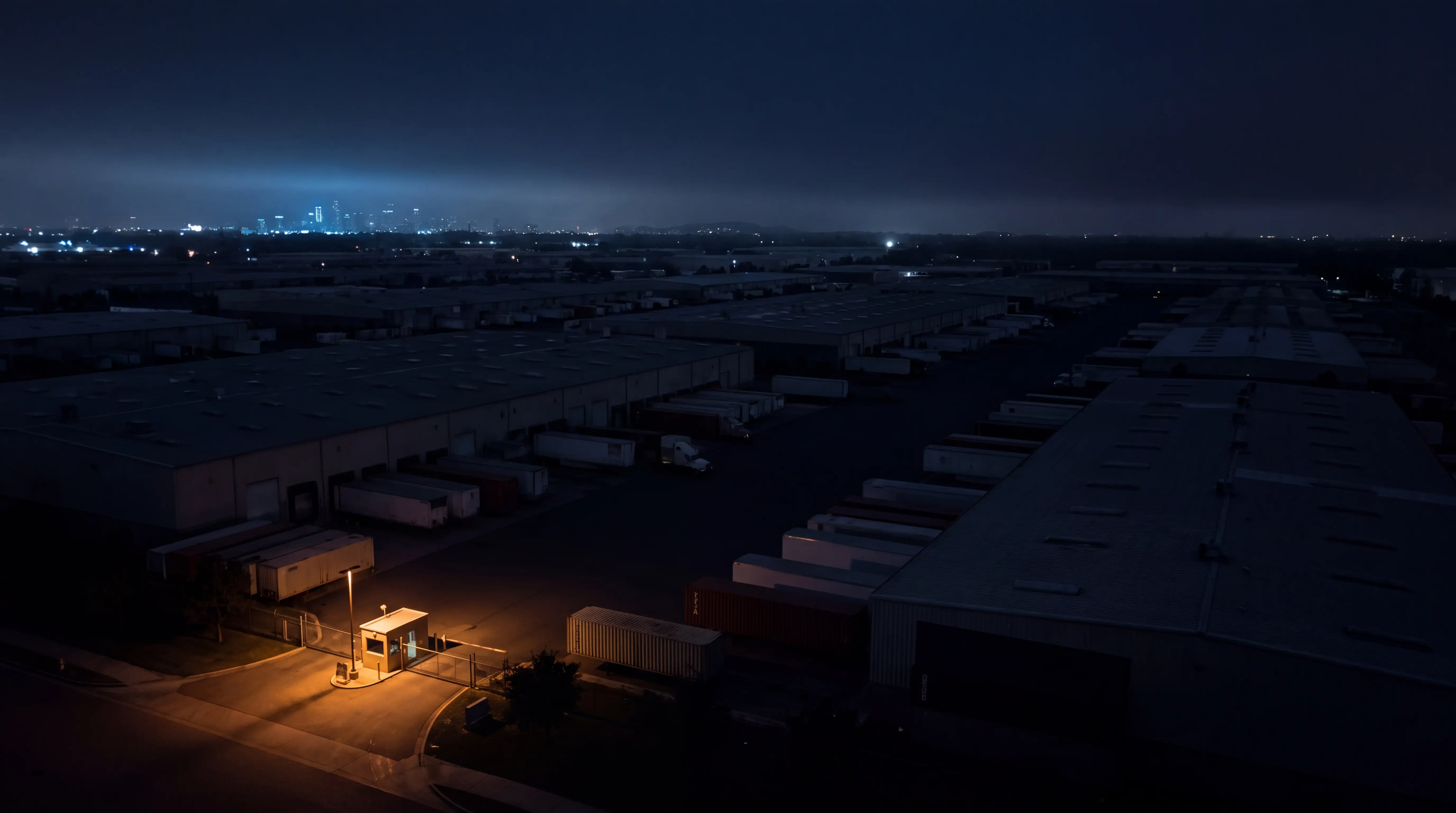 A large industrial estate at night with a single lit gate; everything else sits in darkness.